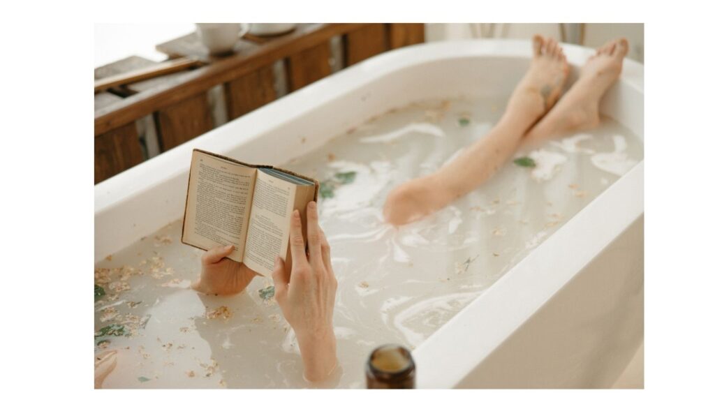 Žena leží ve vaně s bylinkami s kniho v ruce.