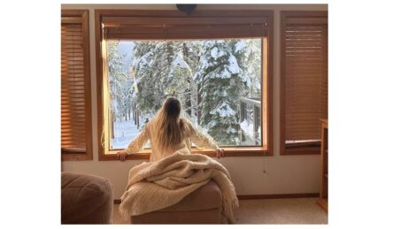 Žena se dívá z okna do zasněžené krajiny.