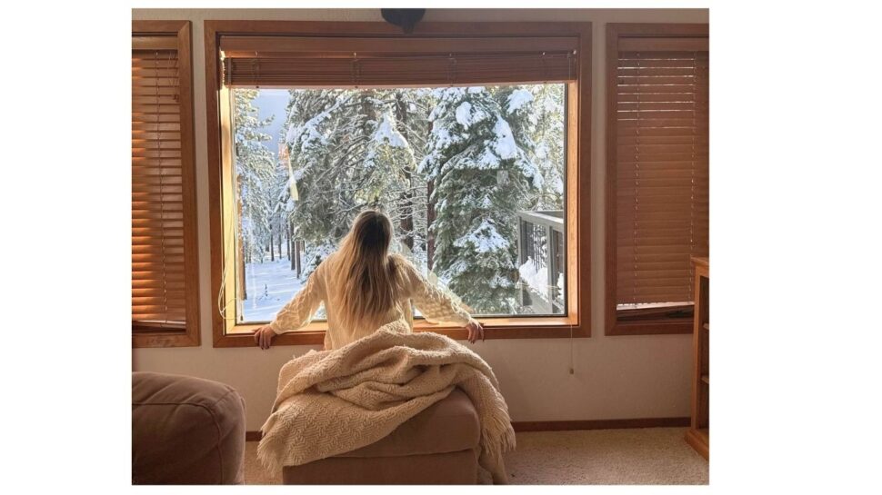 Žena se dívá z okna do zasněžené krajiny.